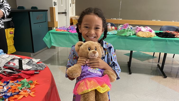Girl patient hold brown teddy bear and smiles at camera