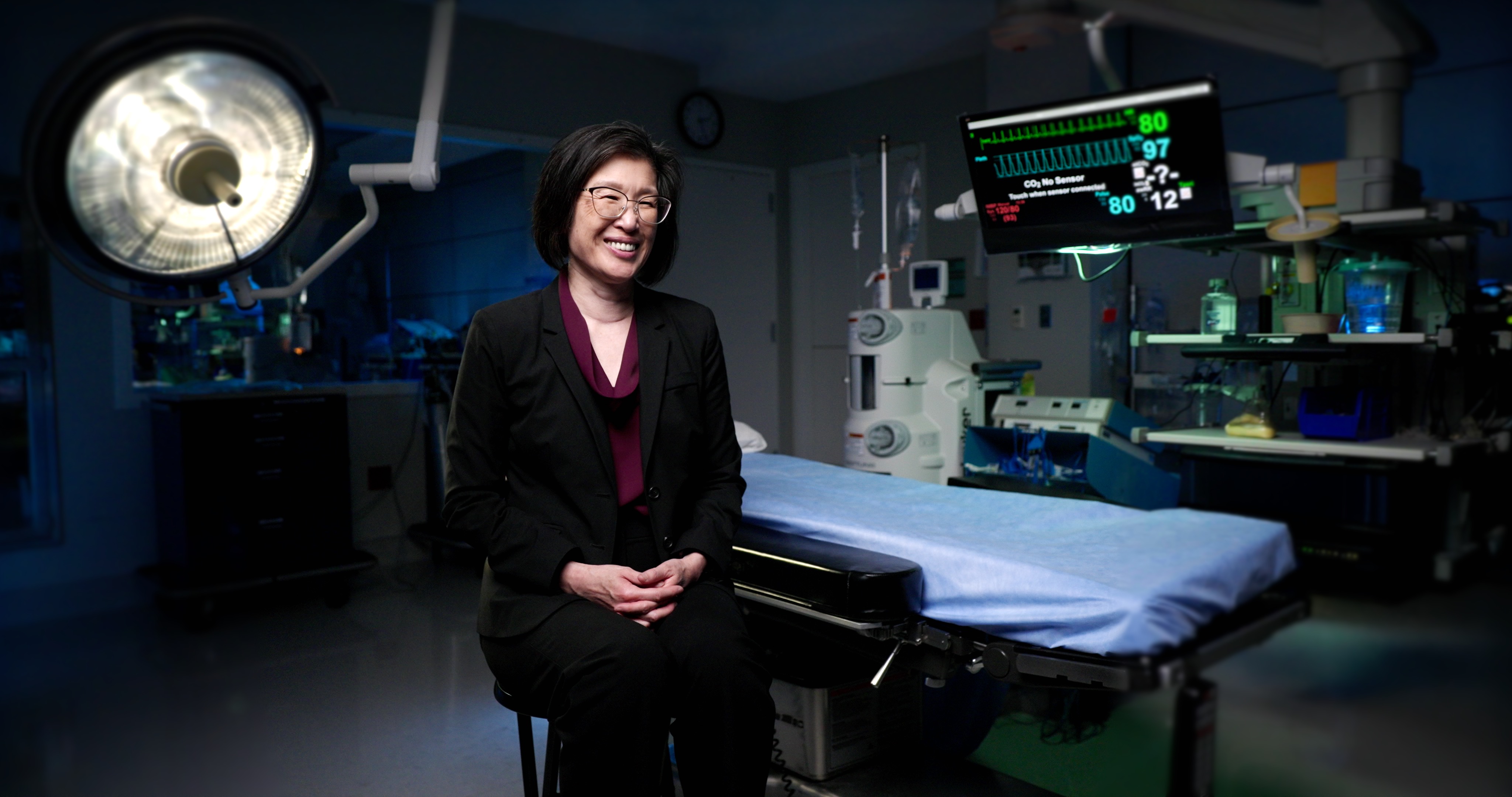 A doctor in all black sits in an operating room for an interview