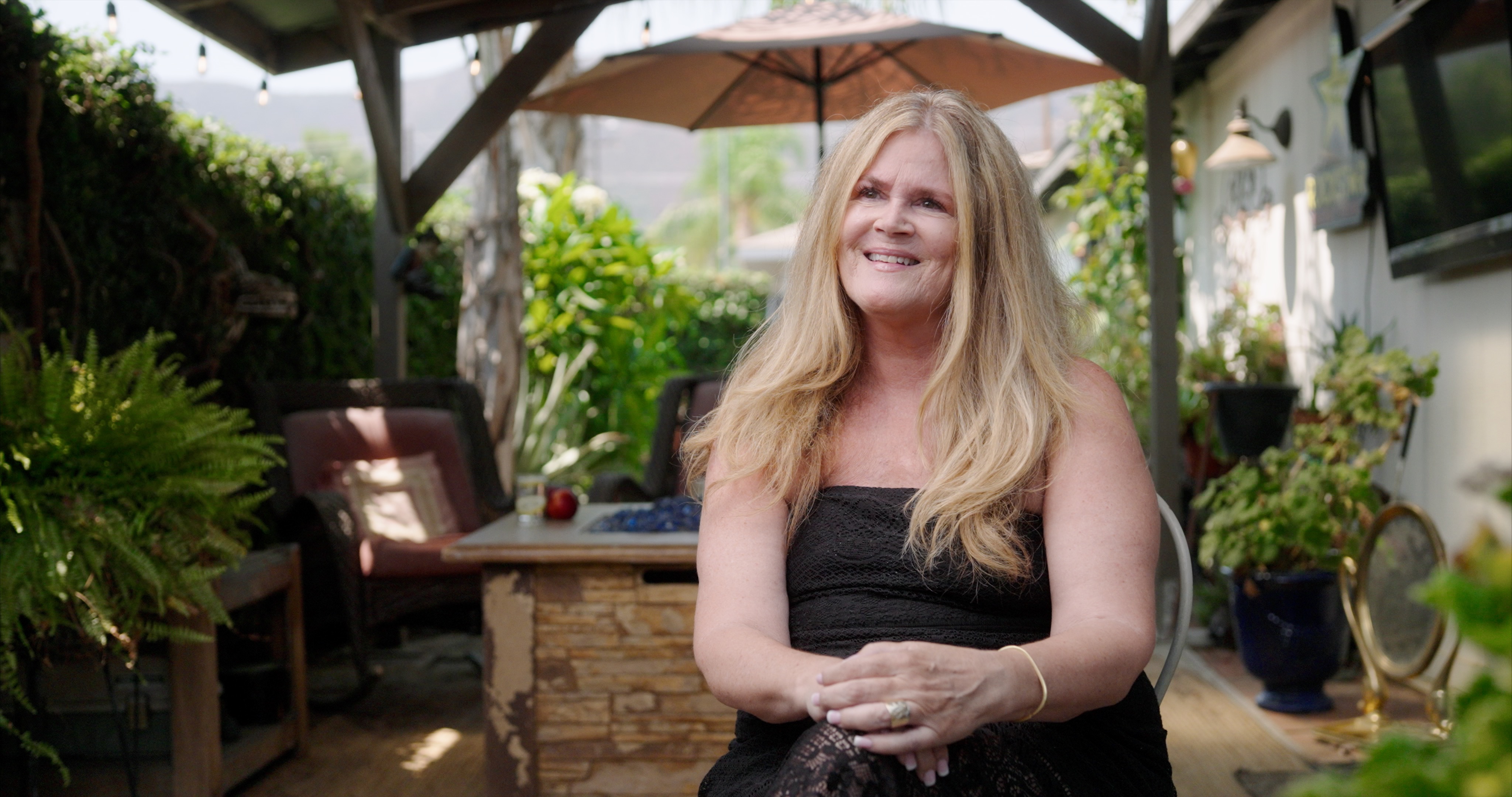 A woman in a black dress sits outside during an interview