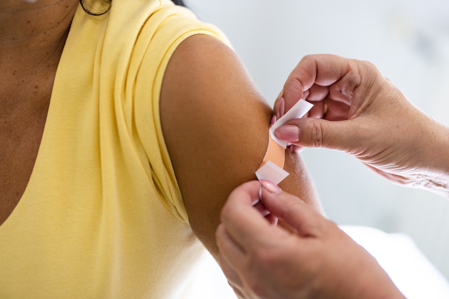 Doctor hands put a bandaid on a woman in a yellow shirt