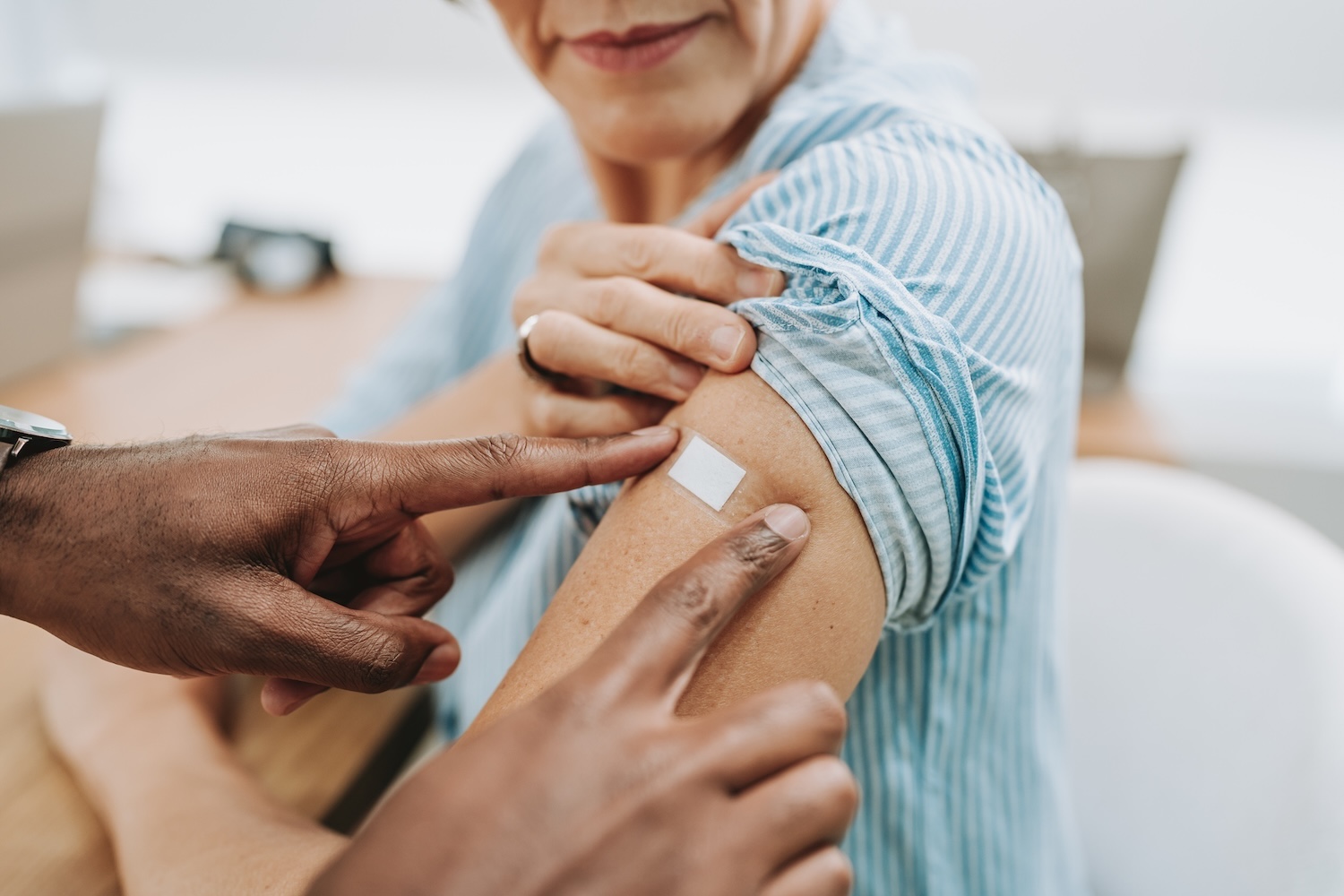 Doctor hands put a bandaid on a woman in a blue shirt