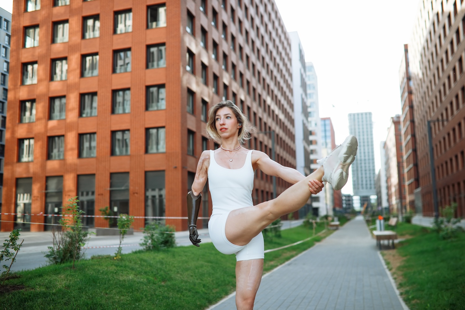 Active lifestyle: middle-aged woman with prosthetic arm stretching legs during city run, pulling knee 