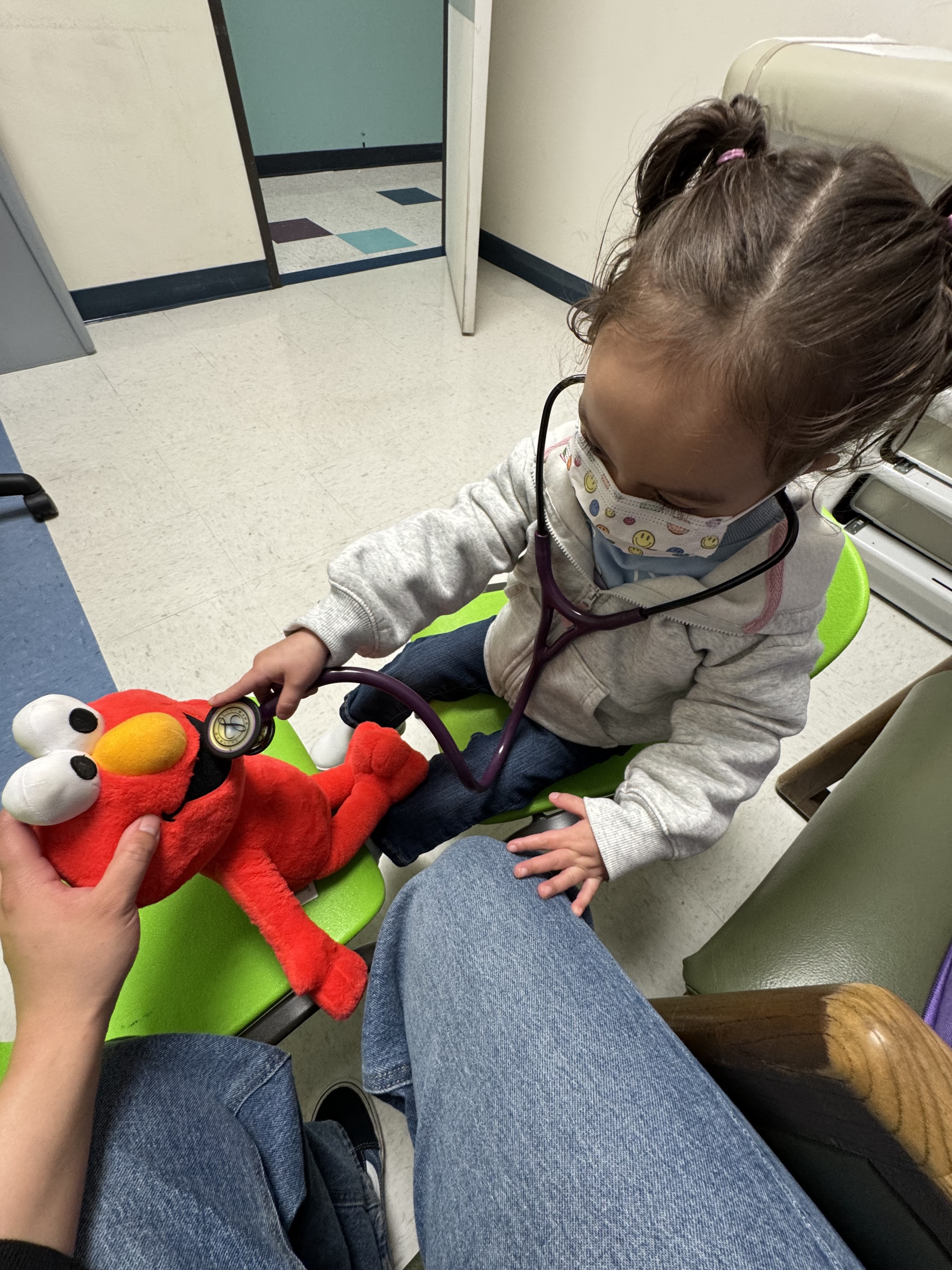 Alaia in clinic using stethoscope on Elmo