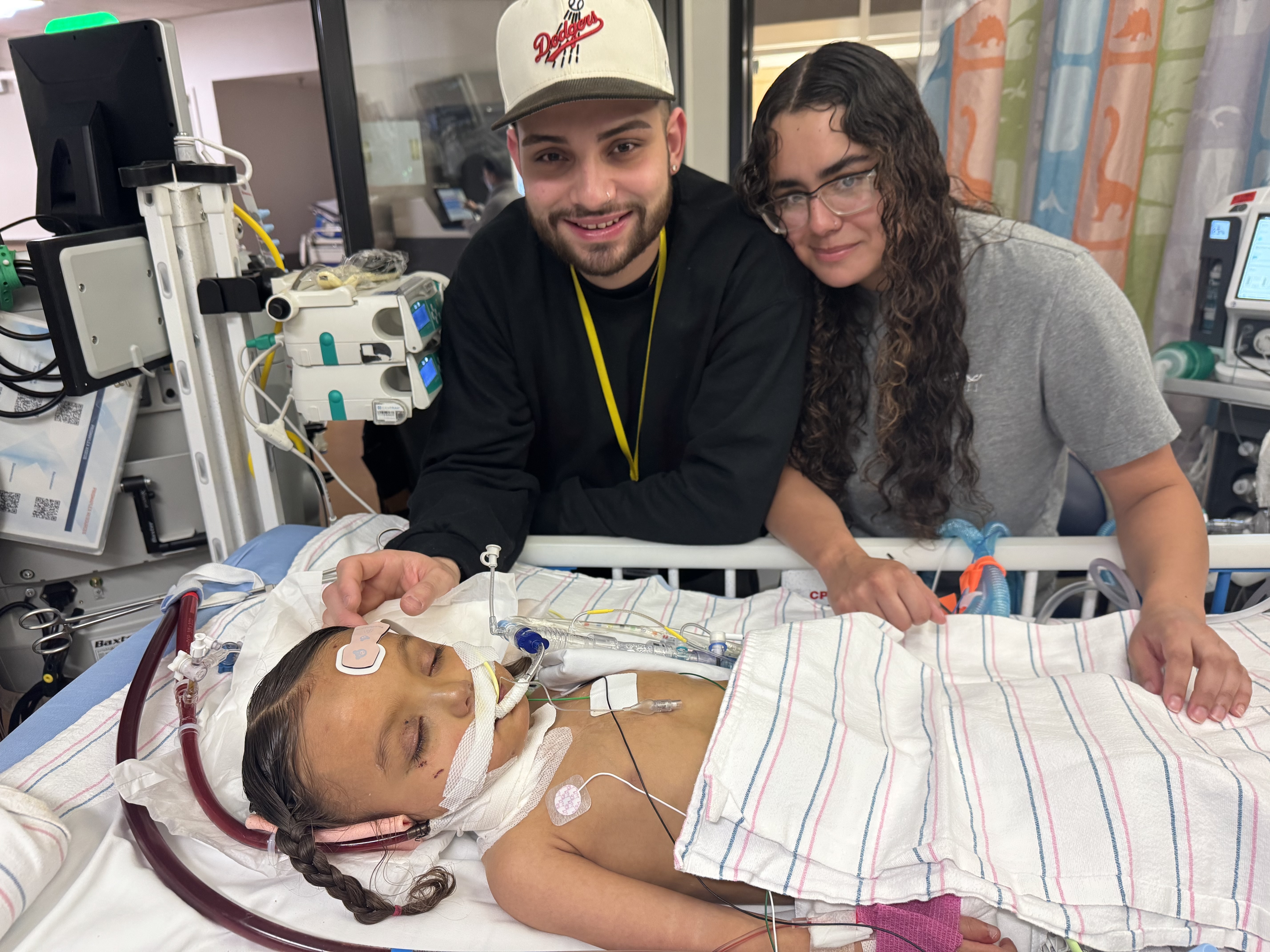 Alaia in hospital bed asleep with parents standing next to her