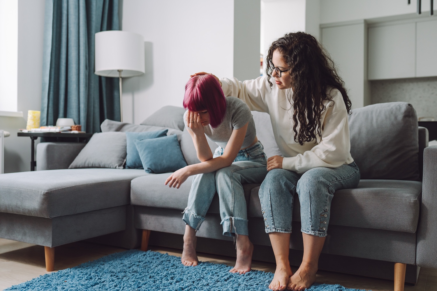 Teenage girl covering her face and crying on a couch, while her mother stroking her on a head