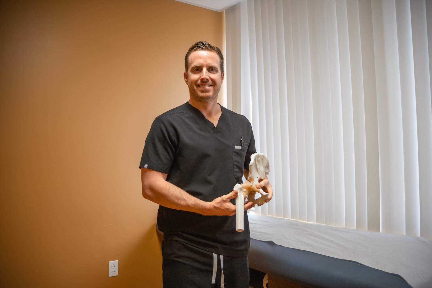 Doctor in black scrubs holds a model of a hip bone