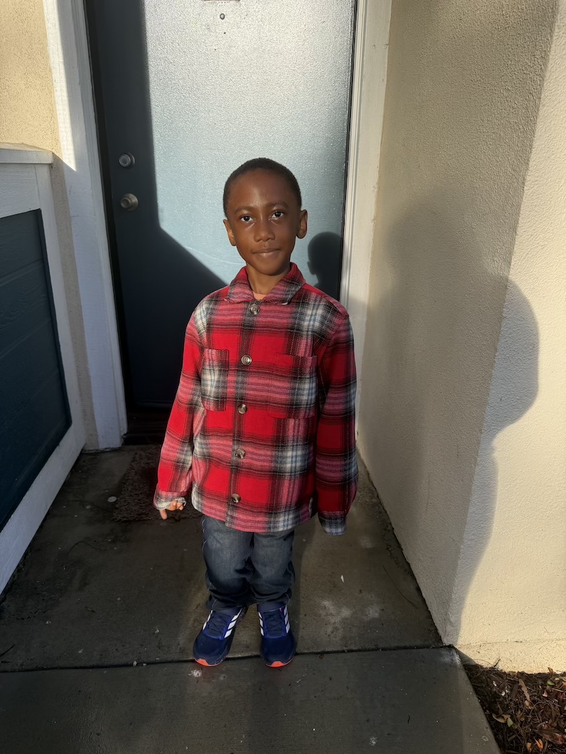 Young boy in a plaid shirt with straight legs smiles at the camera
