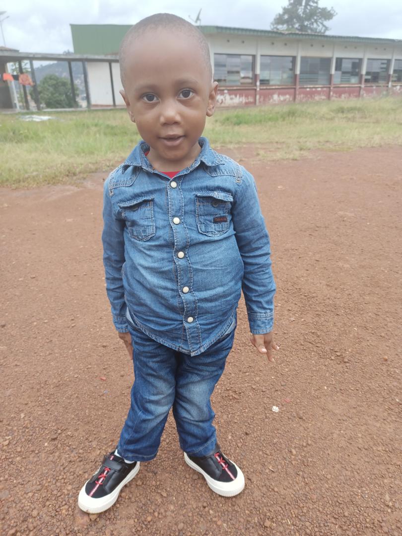 Young boy in a blue shirt and jean with knocked knees smiles at the camera
