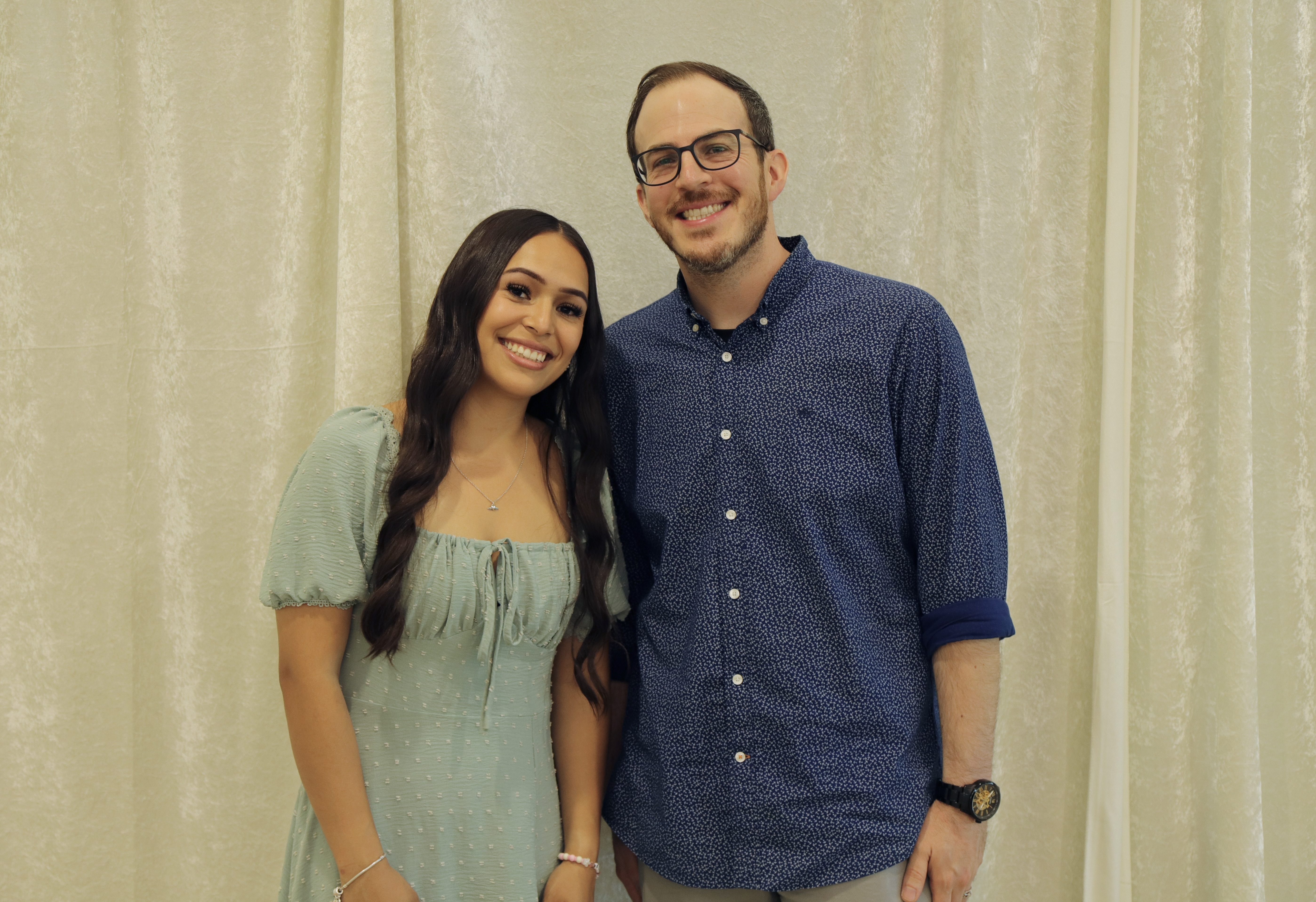 a woman and man smile and pose in front of an ivory backdrop 
