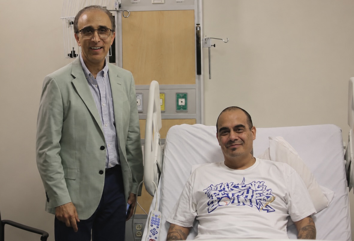 a man stands next to a man in a hospital bed