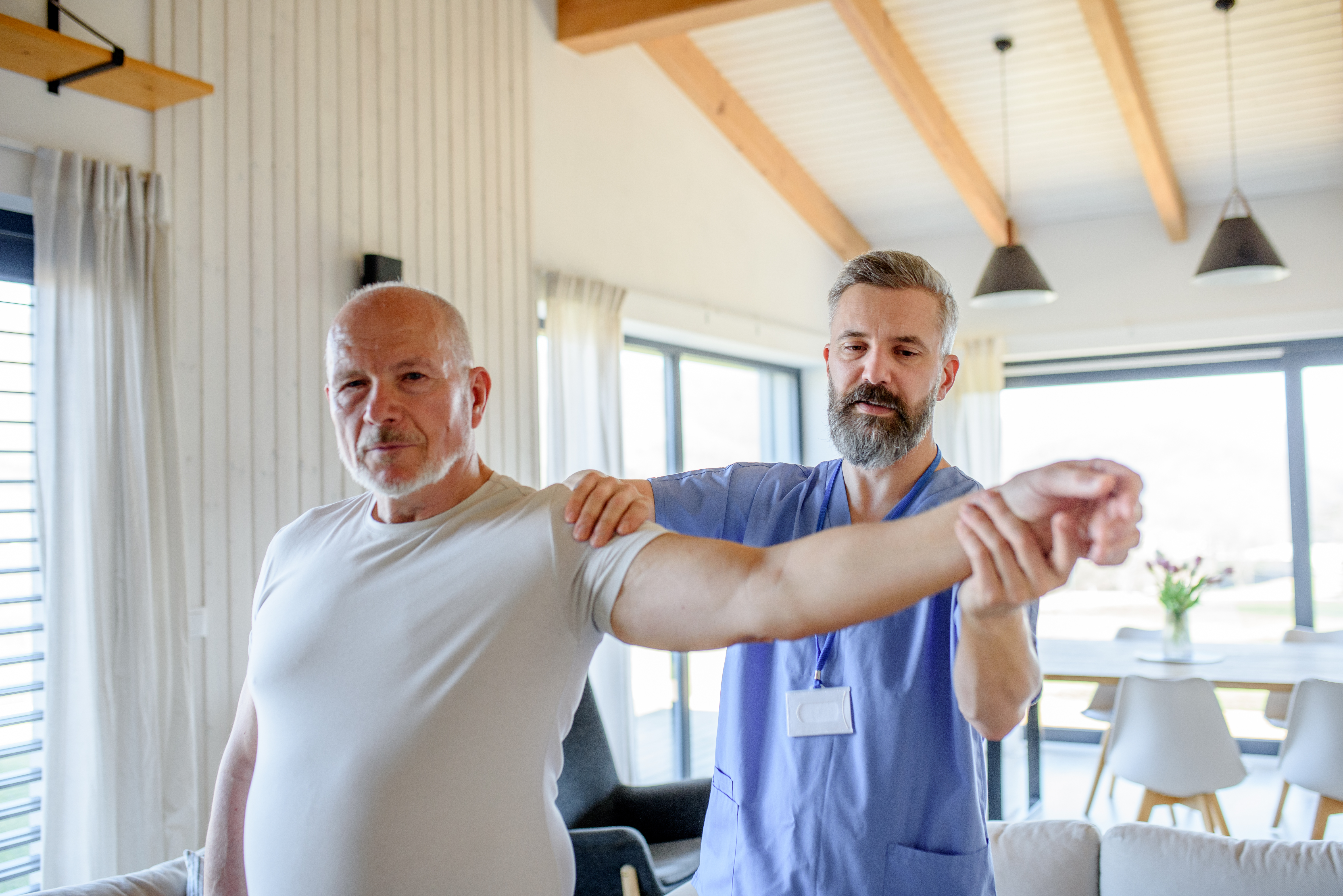 Physiotherapist helping man with rehabilitation exercises at home.