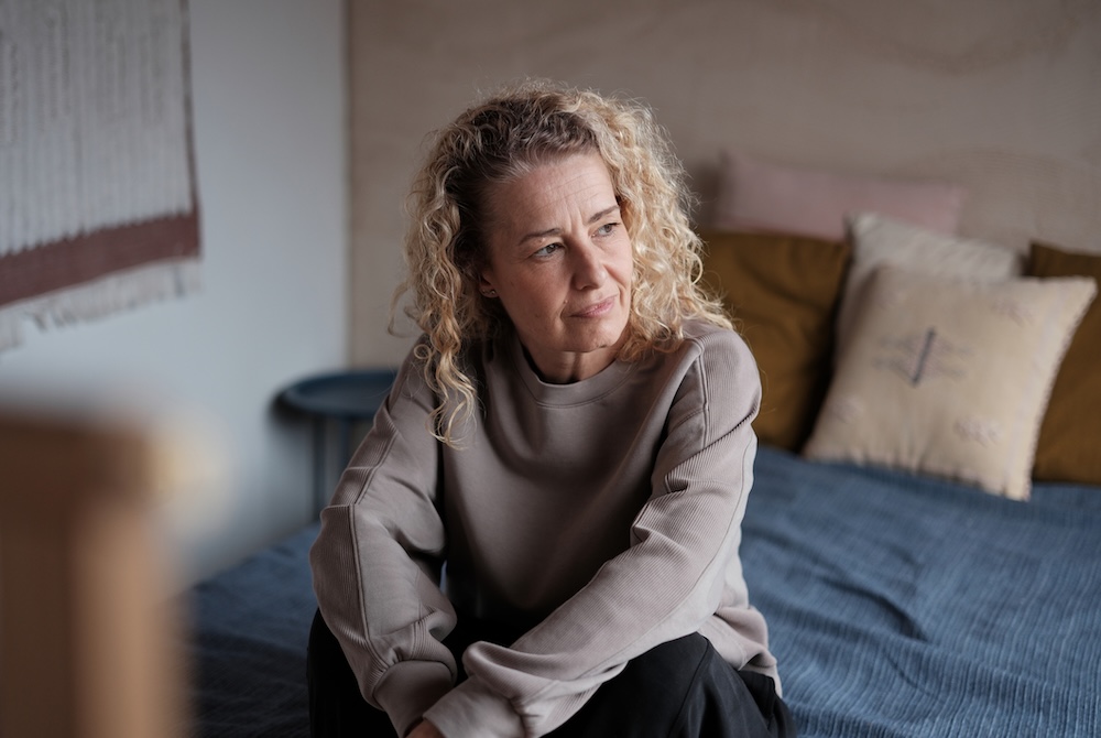 Woman sits on a bed looking sad