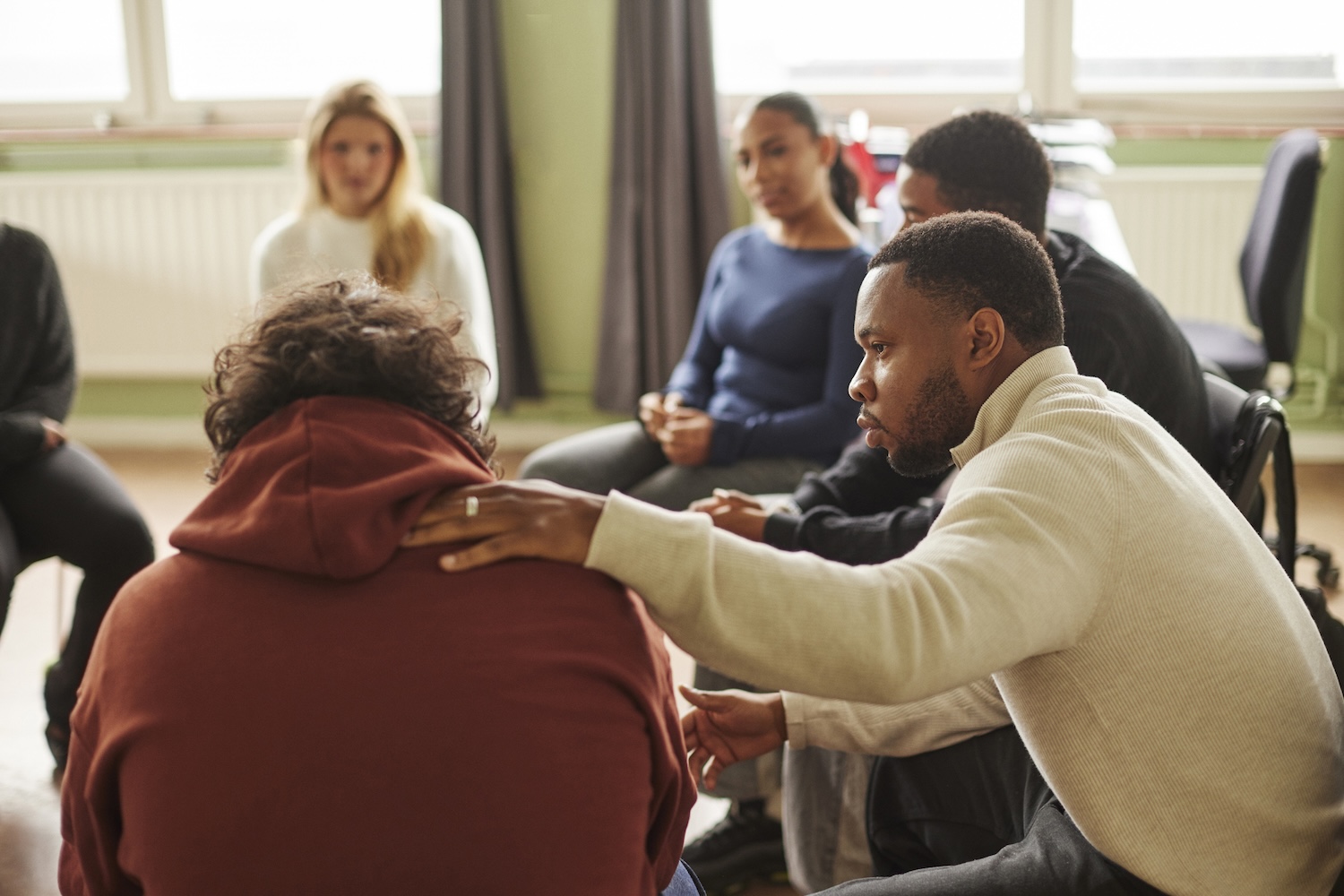 A man puts a hand on the shoulder of someone in a group therapy session