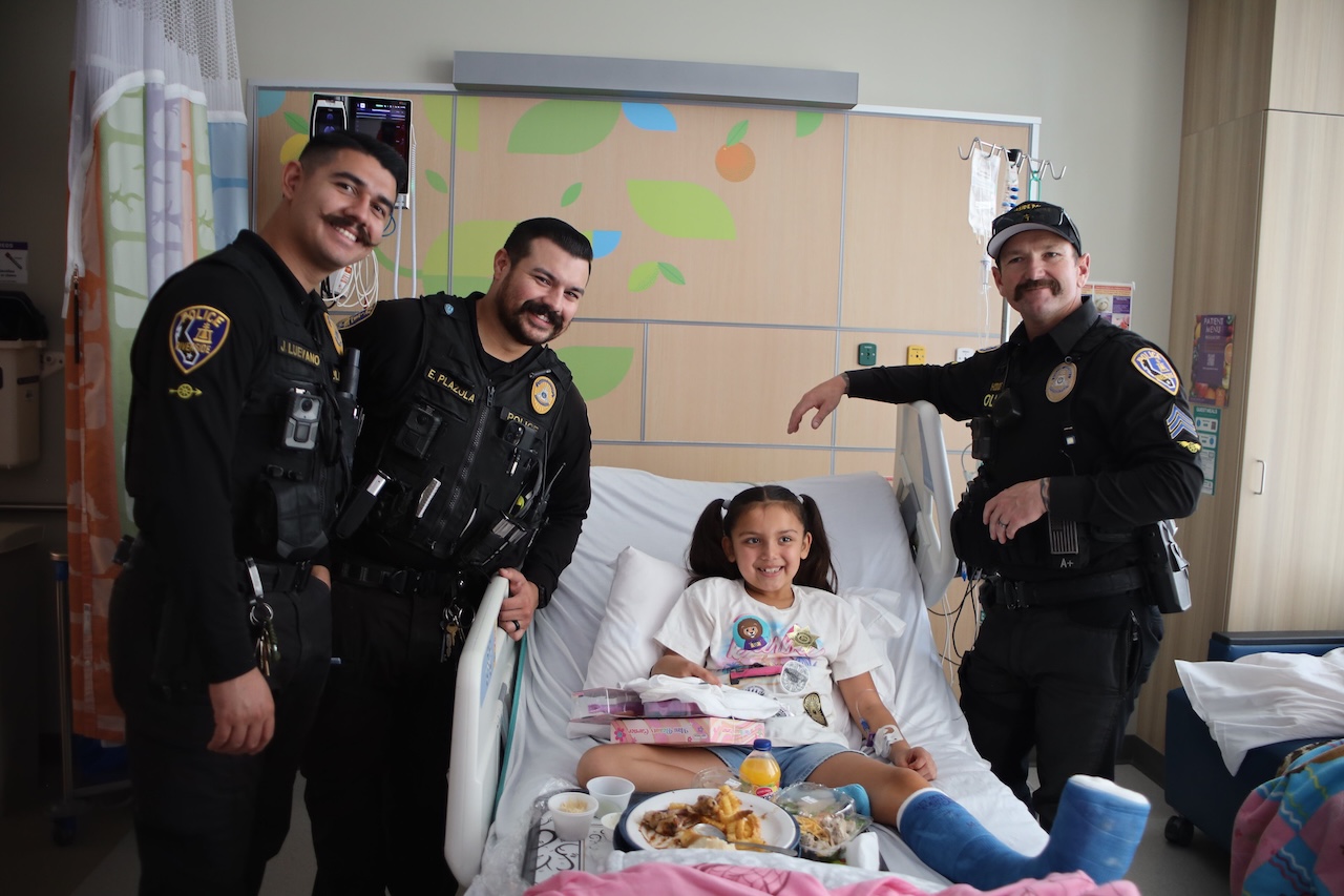 officers pose for picture with patient in hospital bed