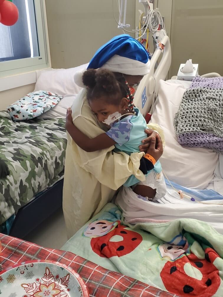 Young Black girl hugging caregiver in a hospital room