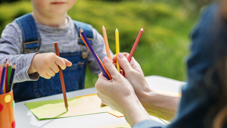 Child holding color pencils and drawing acorss from adult