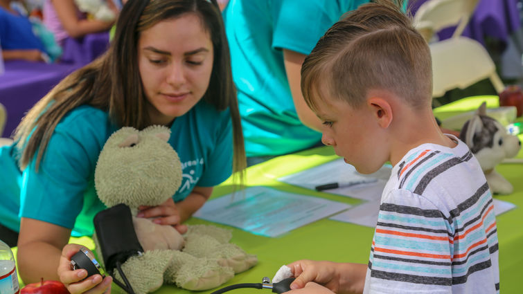 Young woman across table from young boy with teddy bear between them