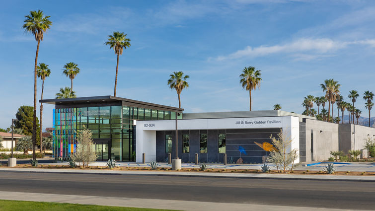 wide shot of concrete and dichroic glass building framed by beautiful blue sky and picturesque palm trees