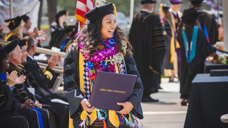 Female graduate in cap and gown wearing floral lei after accepting degree.