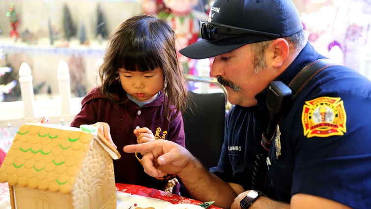 Firefighter helps young girl decorate gingerbread house