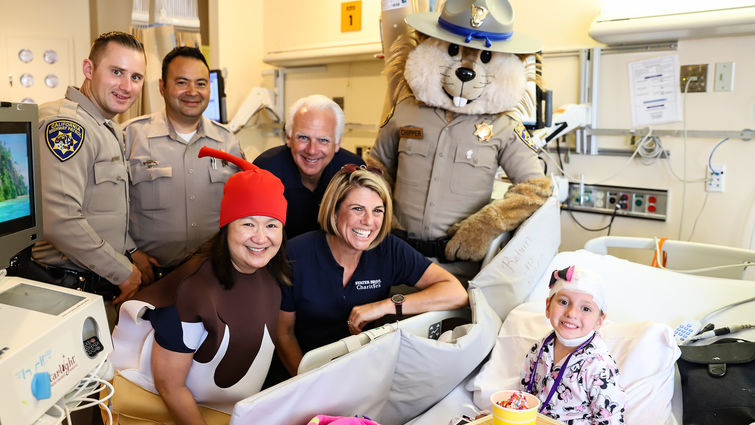 visitors pose by bedside of young female patient for photo