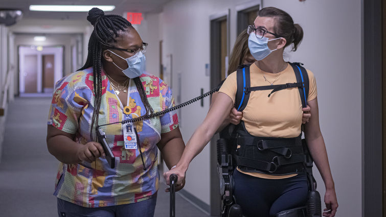 Woman walking down the hall with rehabilitation equipment being helped by another woman