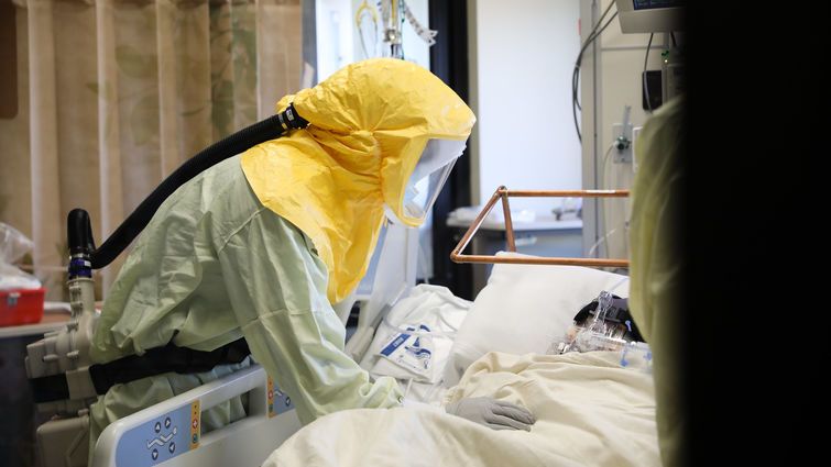 Physician wearing personal protective equipment leans over a COVID-19 patient's bedside in the Loma Linda University Medical Intensive Care Unit.