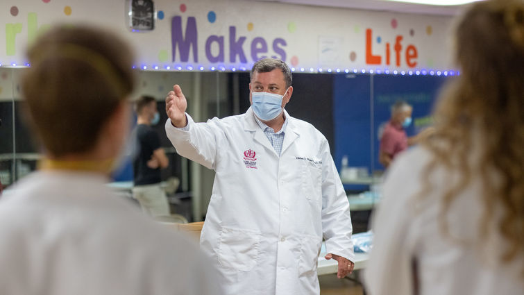 Caucasian doctor stands in white coat with hand outstretched guiding people.