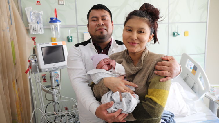 new mother stands with father holding their baby and smiling