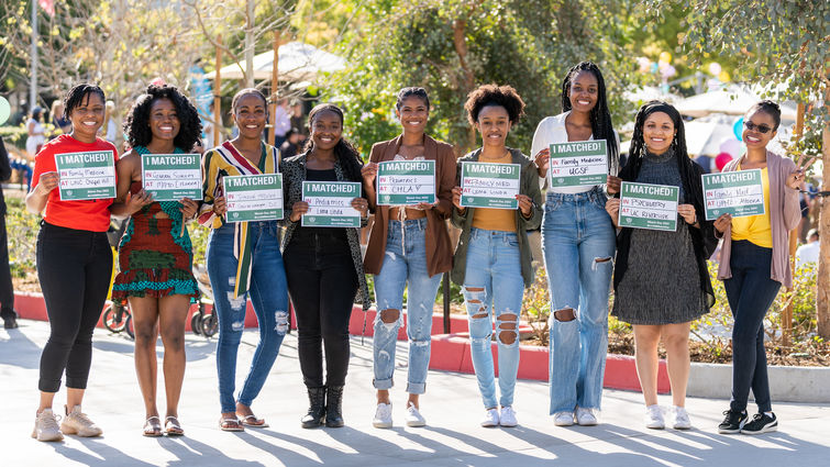 Nine students hold up signs stating where they matched for their residency