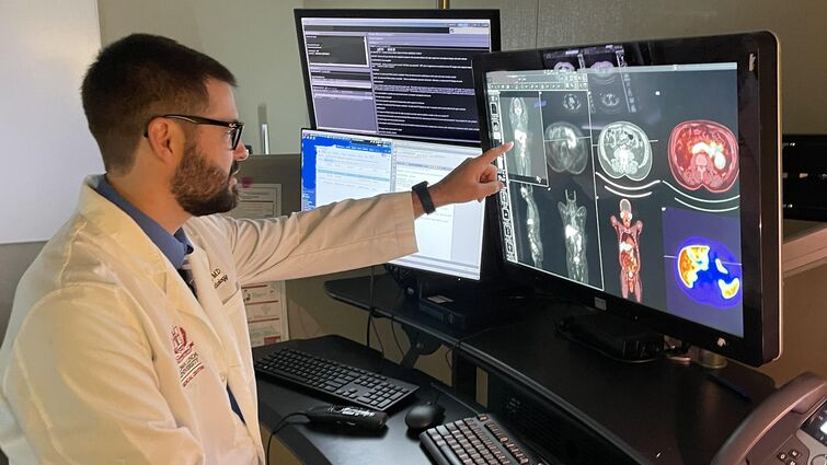 Dr. Peters reviews a patient's positron emission tomography (PET) scan images to identify and treat cancer with targeted precision. A man is looking at a computer screen of a human body scan