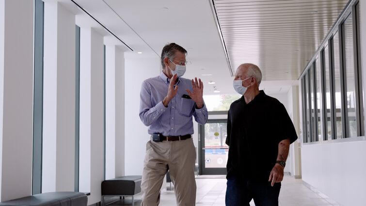 a man is talking with another man as they are walking within a building