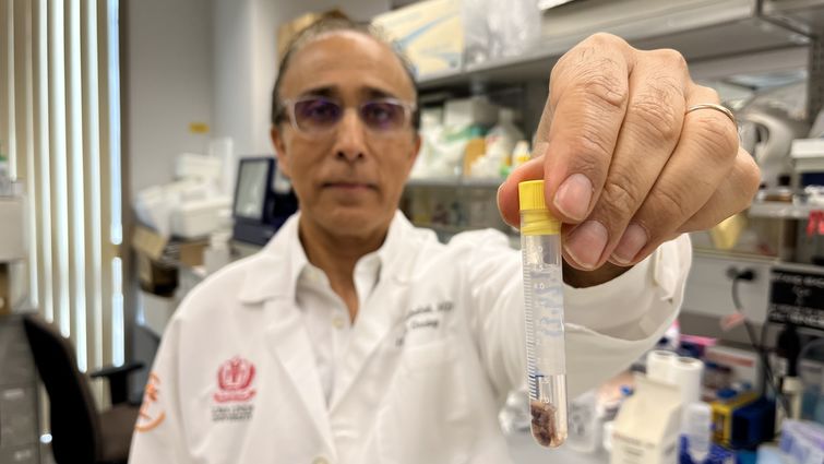 Middle eastern man holding test tube in front of him with cancer cells inside.