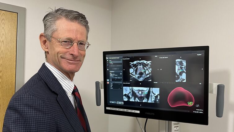 Caucasion man in suit standing next to medical scans related to prostate cancer on a computer monitor