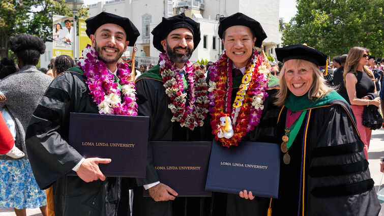 Four college graduates in their cap and gowns, holding their degrees
