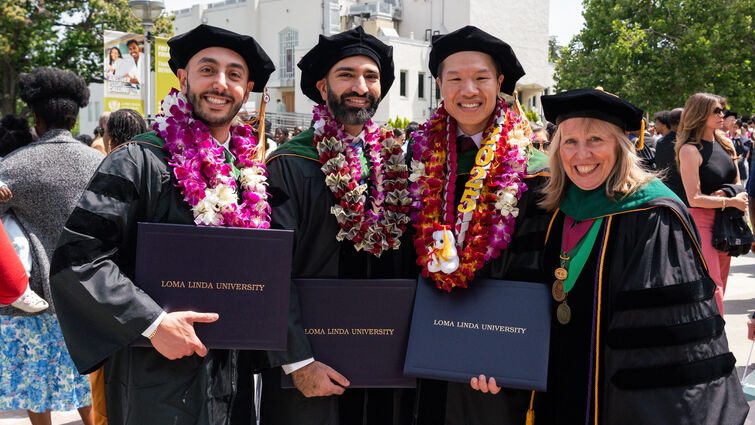 Four college graduates in their cap and gowns, holding their degrees
