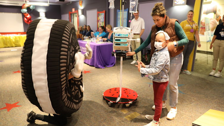 Young patient stands next to her mom and interacts with Oreo charactter at Community Day