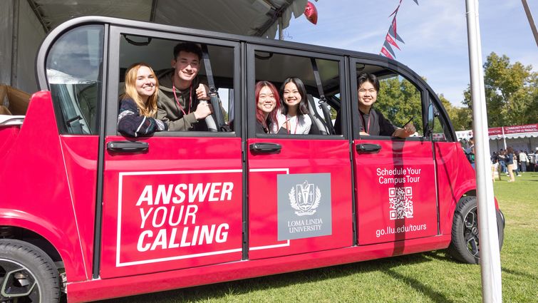 College students in a red, over-sized golf cart, smiling at the camera