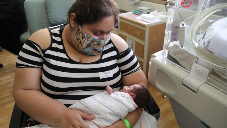 masked mother holds tiny baby