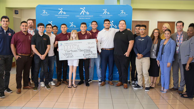 fraternity members stand with patient holding check