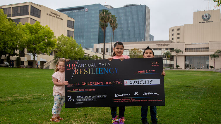 three kids standing in front of hospital with giant check