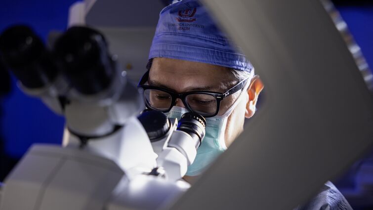 Male doctor in glasses looks through microscope in preparation for brain tumor surgery