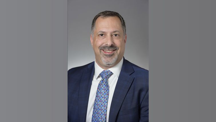 Caucasian male in a navy business suit, with a goatee and mustache