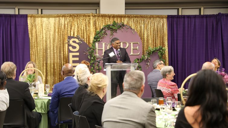 Jeevaka Weerasinghe addresses the audience seated at tables in a large room