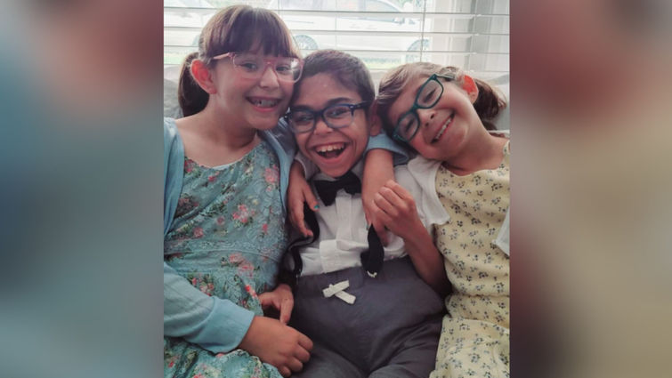 Aiden sitting and smiling with his sisters
