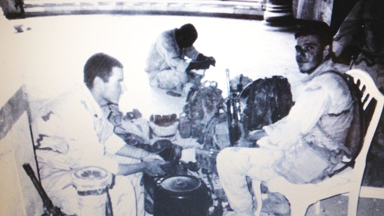 black and white photo showing three military men sitting with combat gear surrounding them.