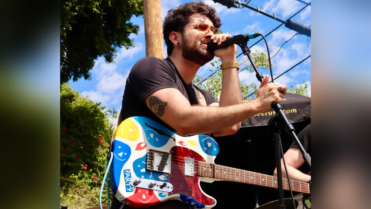 Brandon singing at a microphone with a multicolored guitar strapped over his shoulder