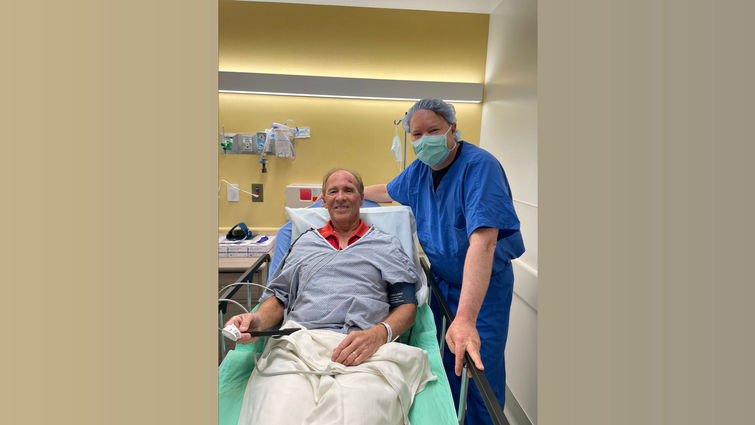 Caucasian man in a hospital bed with his doctor standing beside him in blue scrubs