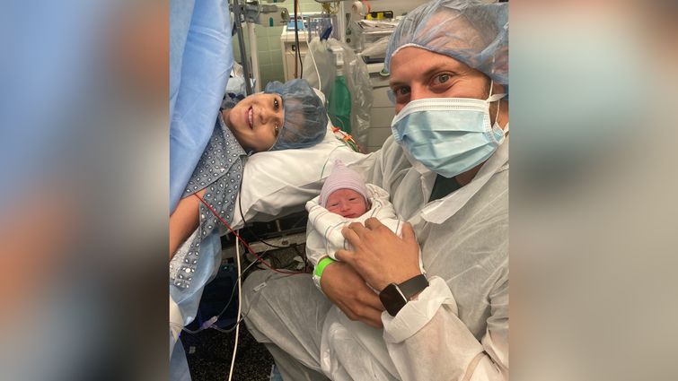 first-time parents smile for photo after a c-section procedure, dad holds baby boy in his arms