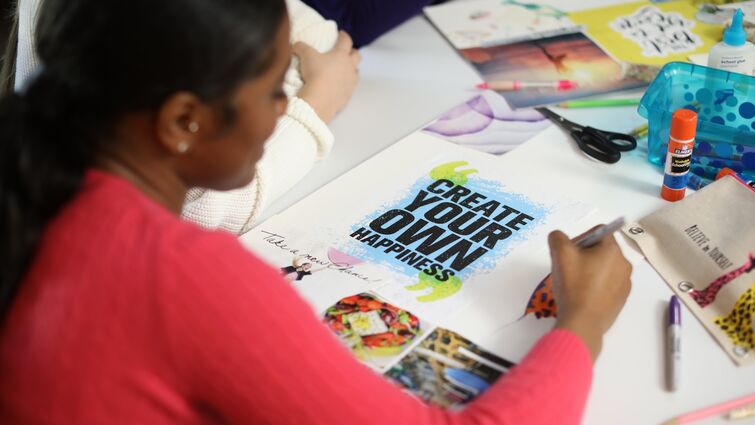 Girl in a red shirt writes on a vision board at a table with crafting supplies